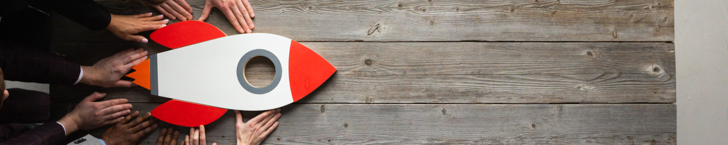 Creative,Business,Team,Sitting,At,Table,With,Startup,Rocket